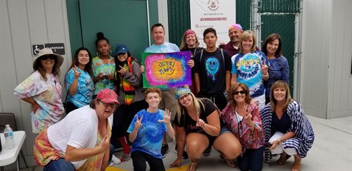group of people wearing tyed-dyed shirts posing in front of a classroom door